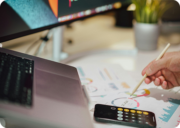 Persona revisando informes gráficos de rendimiento financiero sobre un escritorio junto a una laptop y una calculadora
