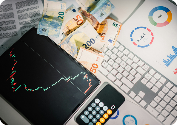 Escritorio de trabajo con billetes en euros, gráficos estadísticos, una tablet mostrando un gráfico bursátil y un teclado