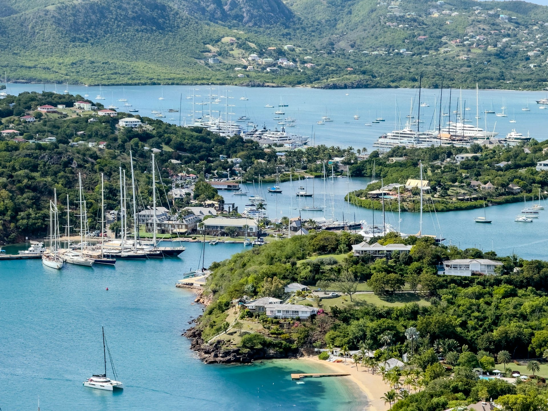 Vista aérea de embarcaciones y yates anclados en una bahía tropical rodeada de colinas verdes.