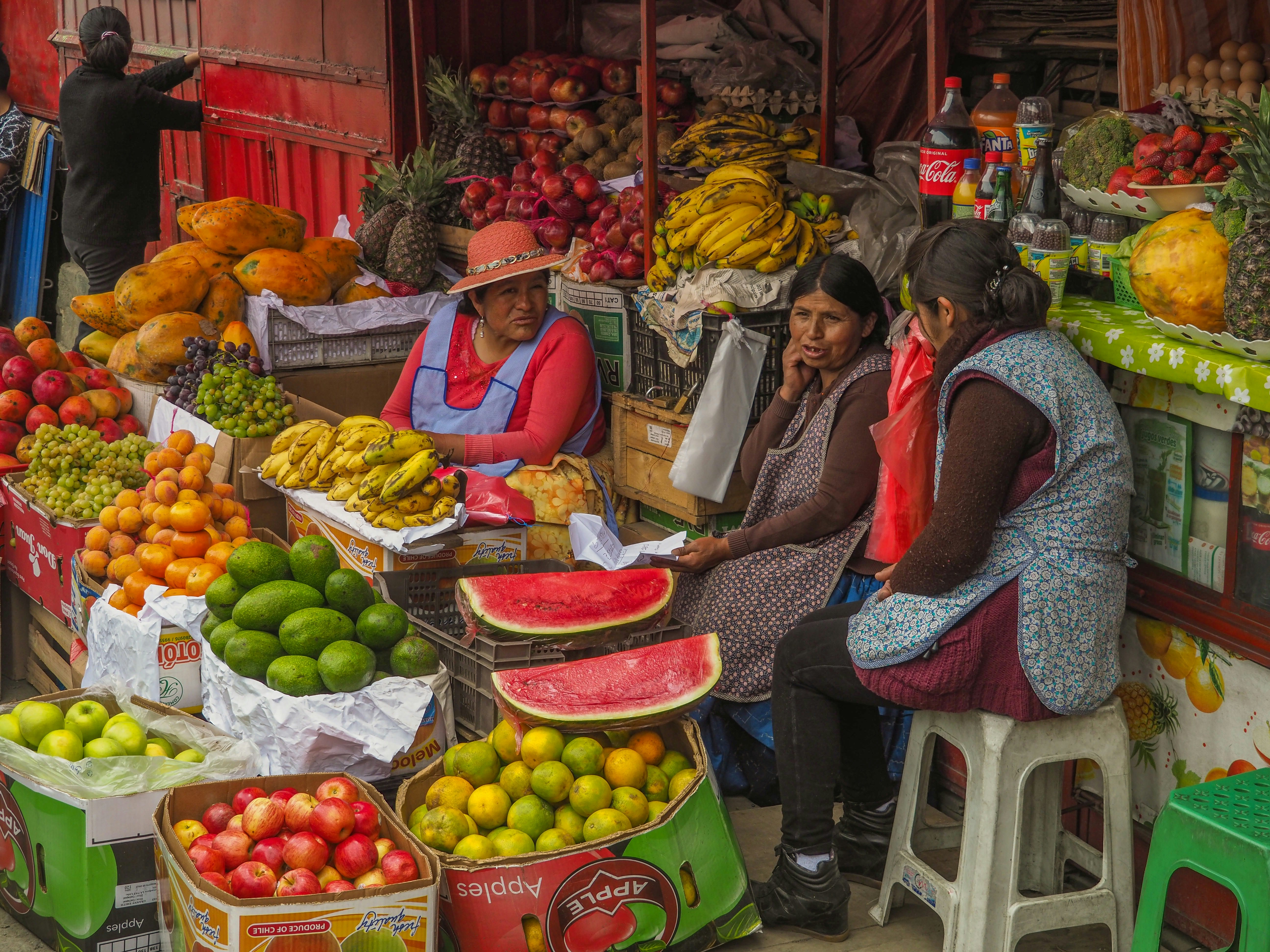 Comerciantes locales vendiendo sandías, mangos y mandarinas en un puesto de mercado al aire libre.