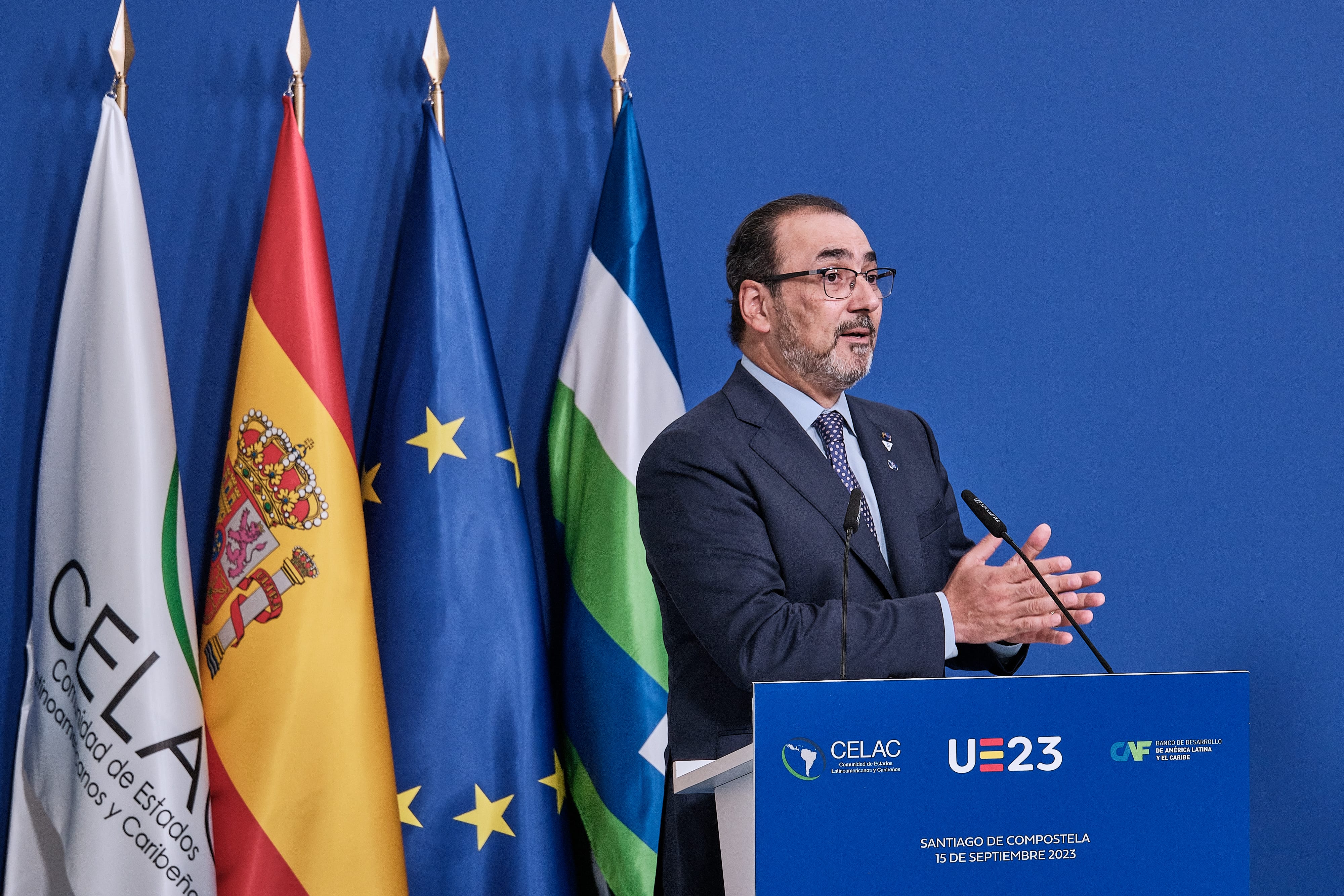 Representante dirigiéndose al público desde un podio frente a las banderas de España y la Unión Europea.