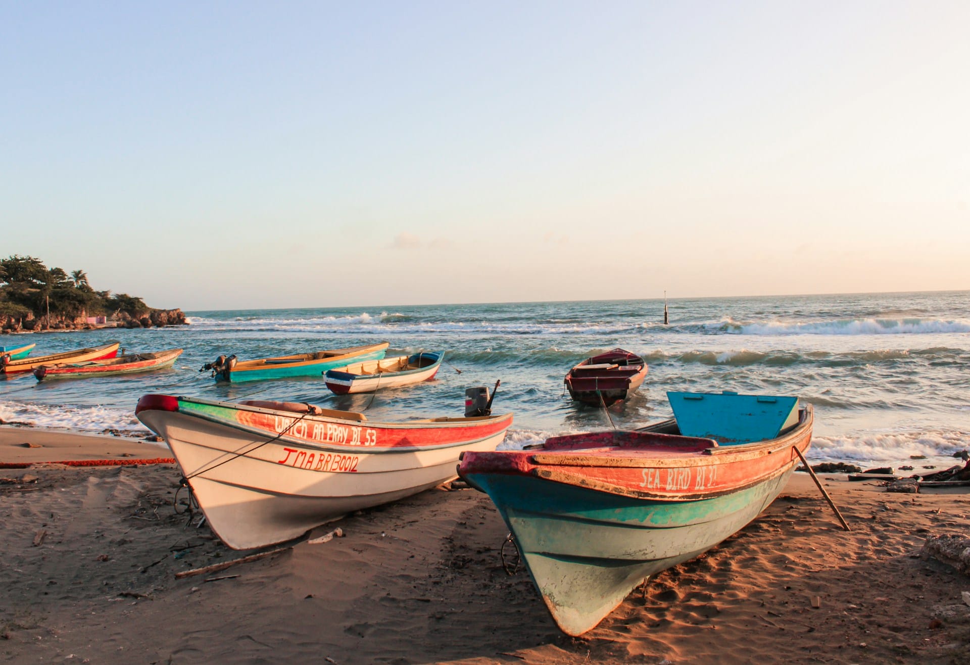 Lanchas pesqueras de madera descansando sobre la arena en una playa costera al atardecer.