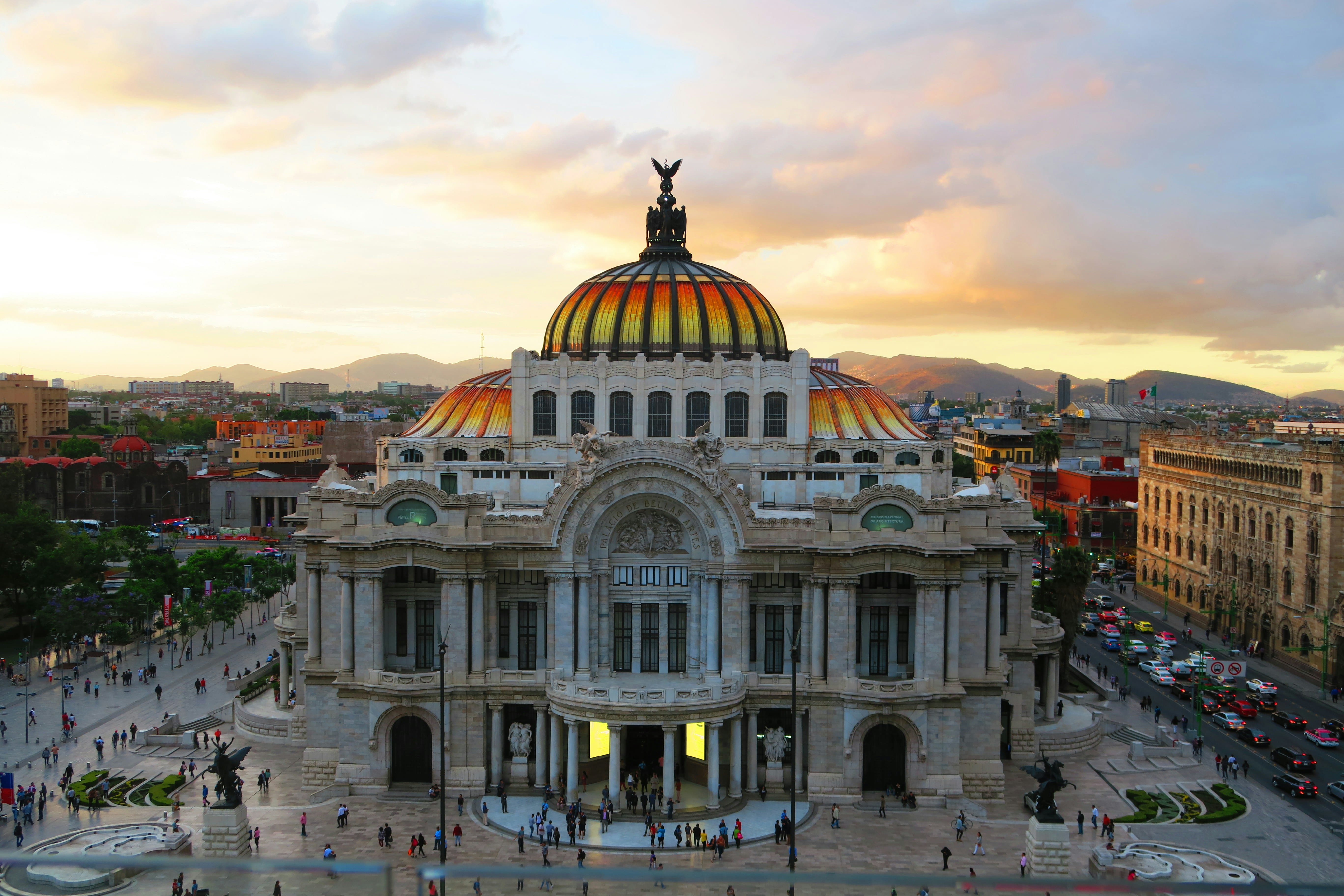 Vista frontal del Palacio de Bellas Artes con su característica cúpula dorada y naranja al atardecer.